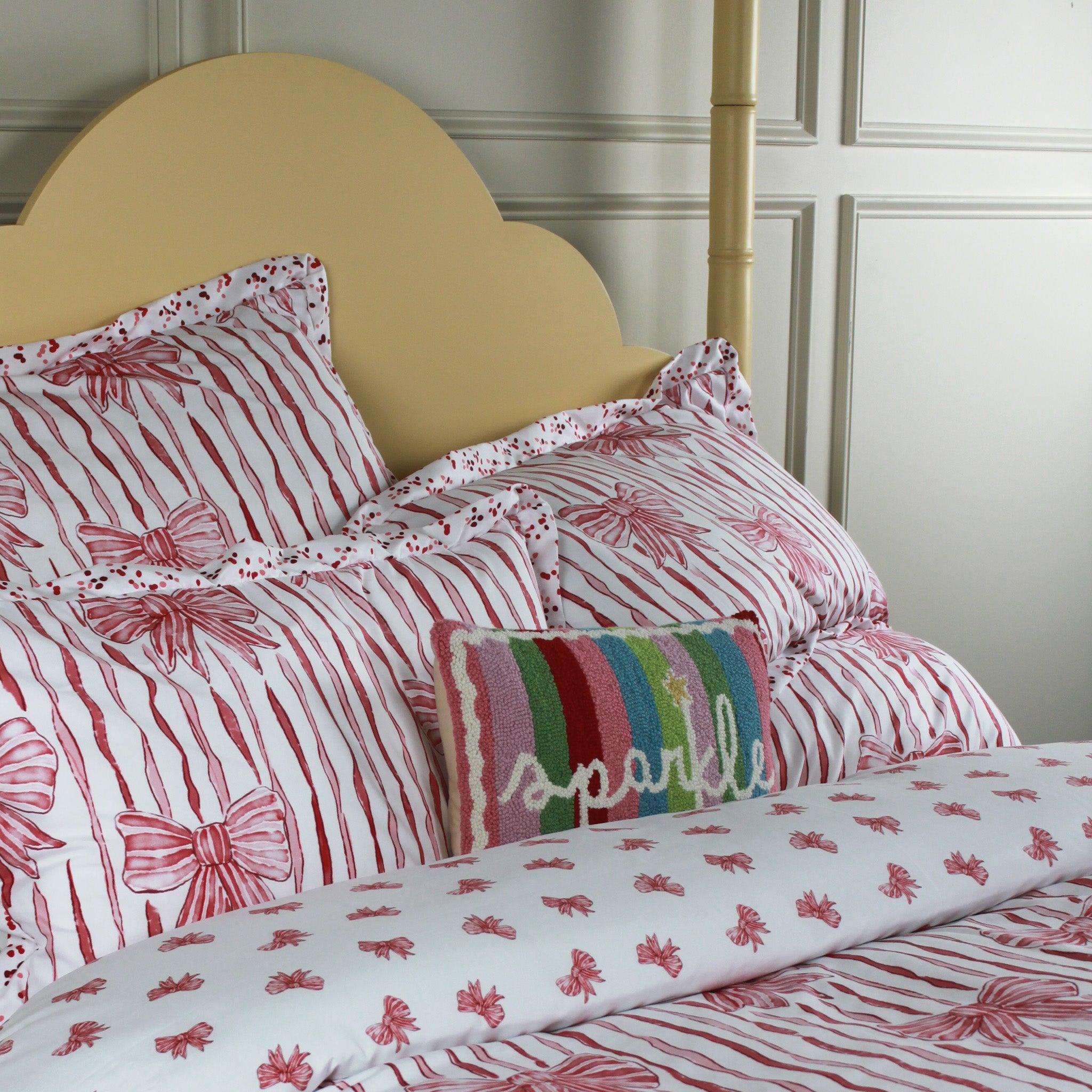 Bed with red and white bow patterned bedding and a colorful pillow.