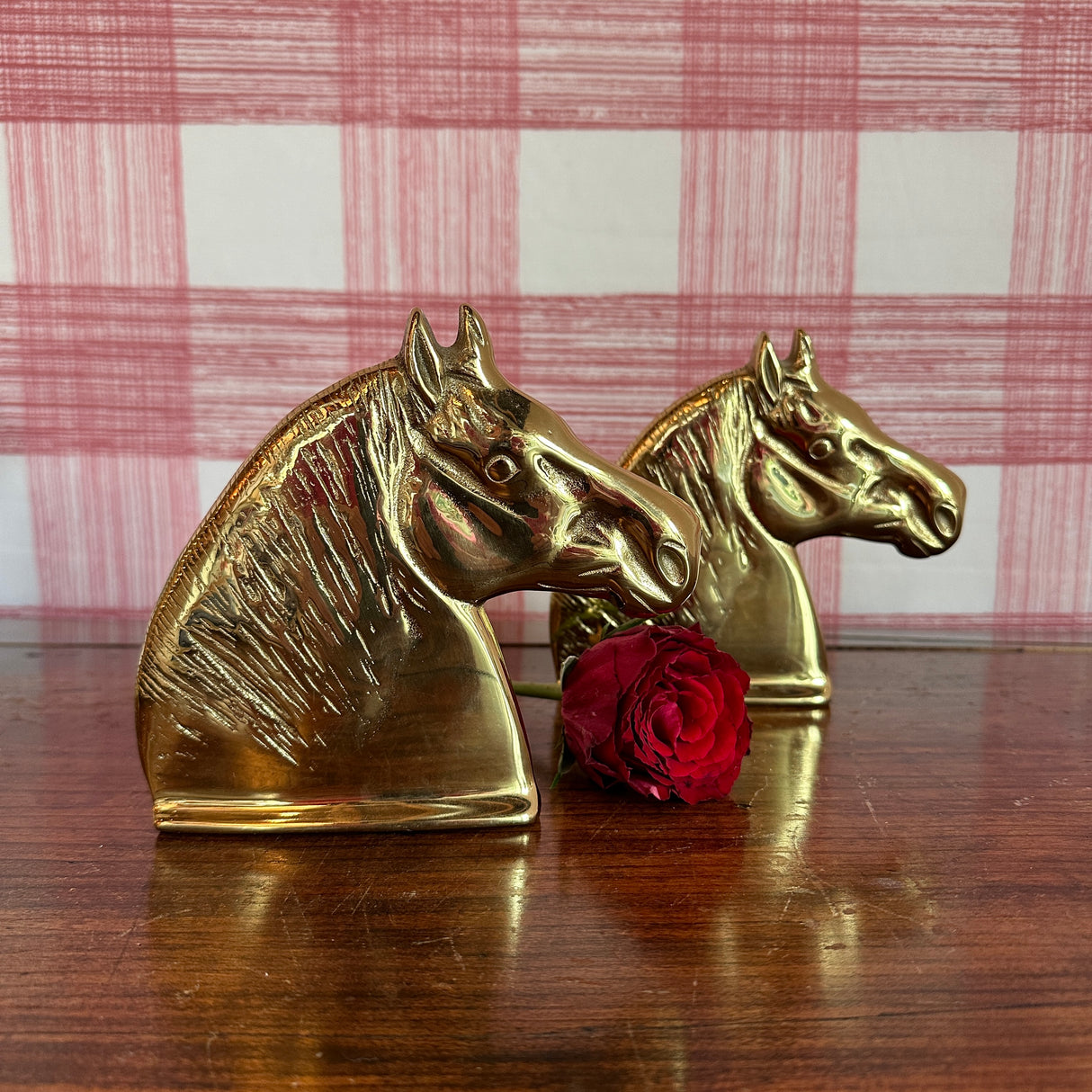 A pair of brass horse book ends with a red rose between them.