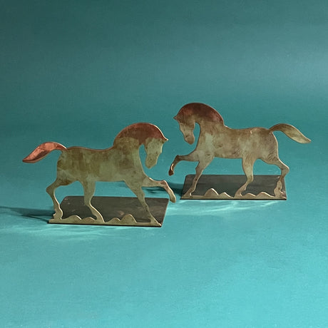 a pair of dancing brass horse bookends on a green background