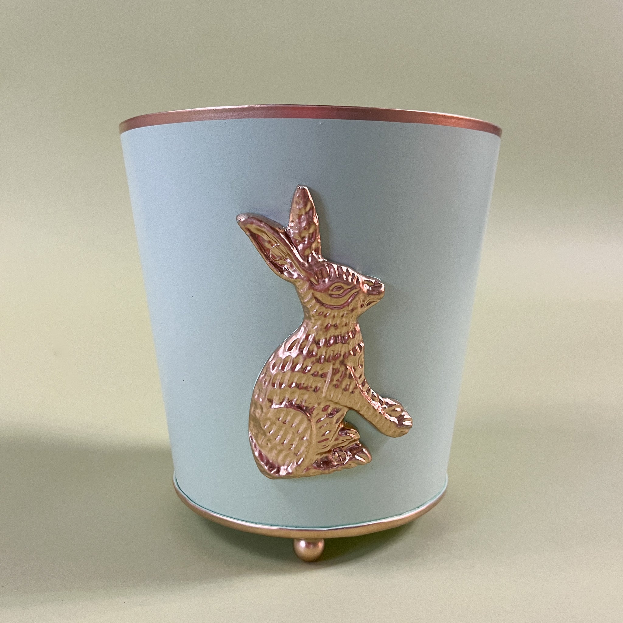 a green tole cachepot with a gold bunny motif and gold rim and feet.