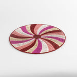 A round rattan christmas placemat with pink, red, white and yellow candy-cane like swirls. 