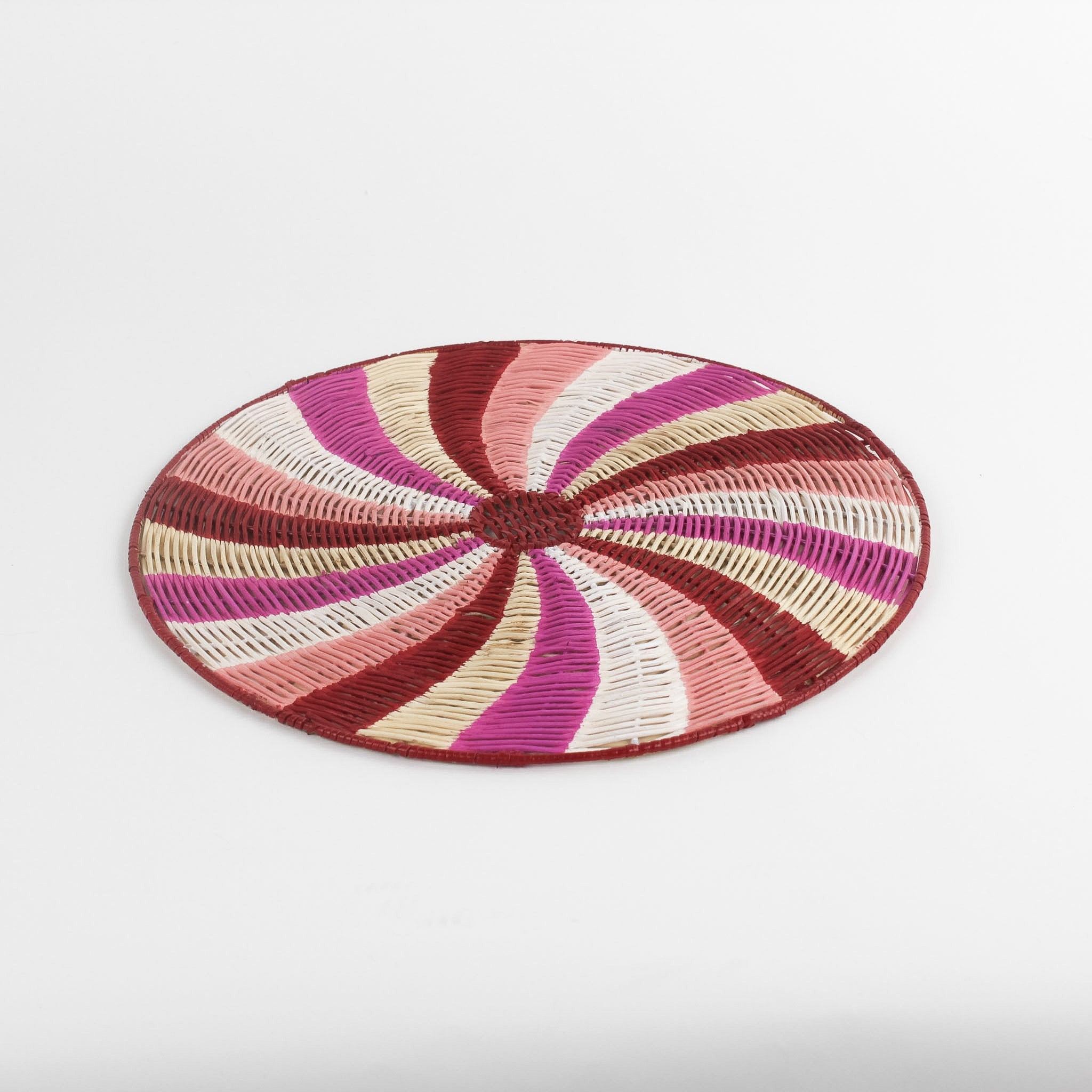 A round rattan christmas placemat with pink, red, white and yellow candy-cane like swirls. 