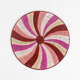 A round rattan christmas placemat with pink, red, white and yellow candy-cane like swirls. 