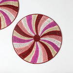 A round rattan christmas placemat with pink, red, white and yellow candy-cane like swirls. 