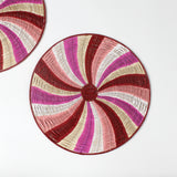 A round rattan christmas placemat with pink, red, white and yellow candy-cane like swirls. 