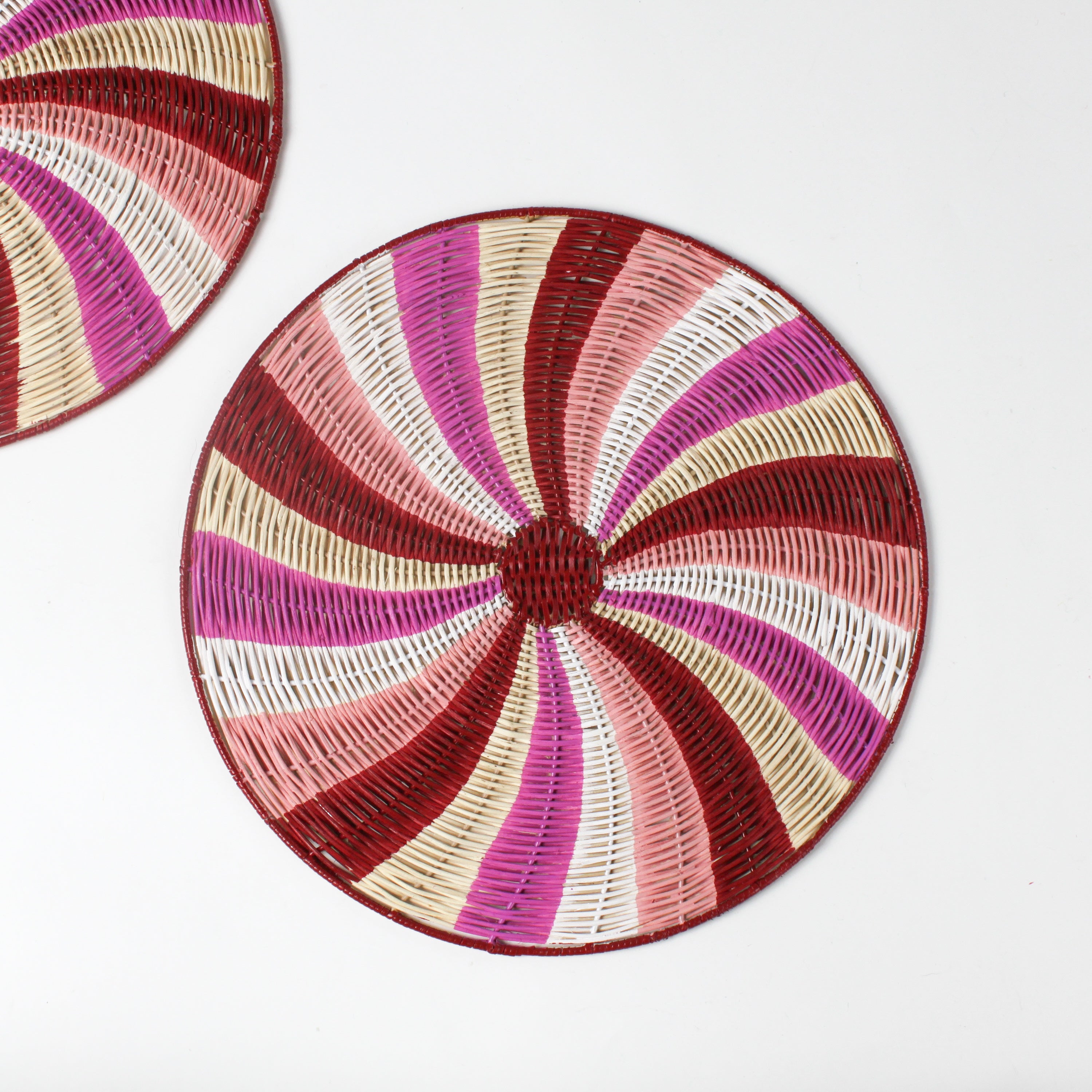 A round rattan christmas placemat with pink, red, white and yellow candy-cane like swirls. 