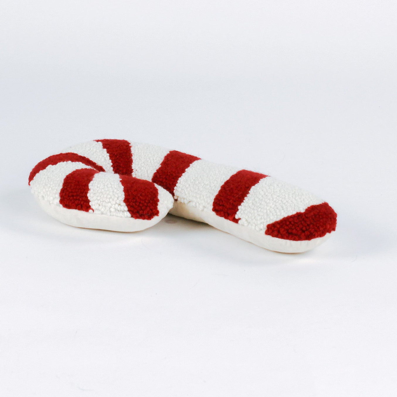 Candy cane–shaped Christmas pillow with red and white stripes, made from a textured hooked wool fabric and laid against a white background.