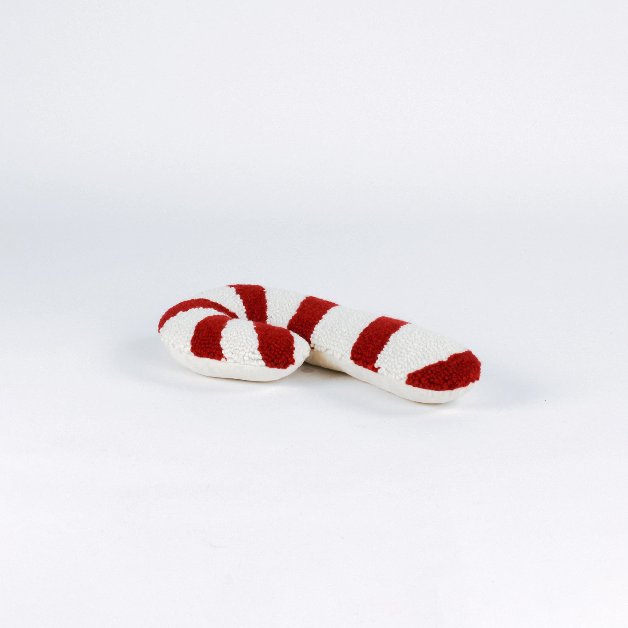 Candy cane–shaped decorative pillow with red and white stripes, made from a textured hooked fabric and laid against a white background.