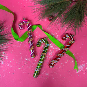 set of three colorful candy cane glass christmas tree ornaments against a pink background 