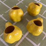 Ceramic pear napkin rings in yellow with green stem, styled with patterned cloth napkins