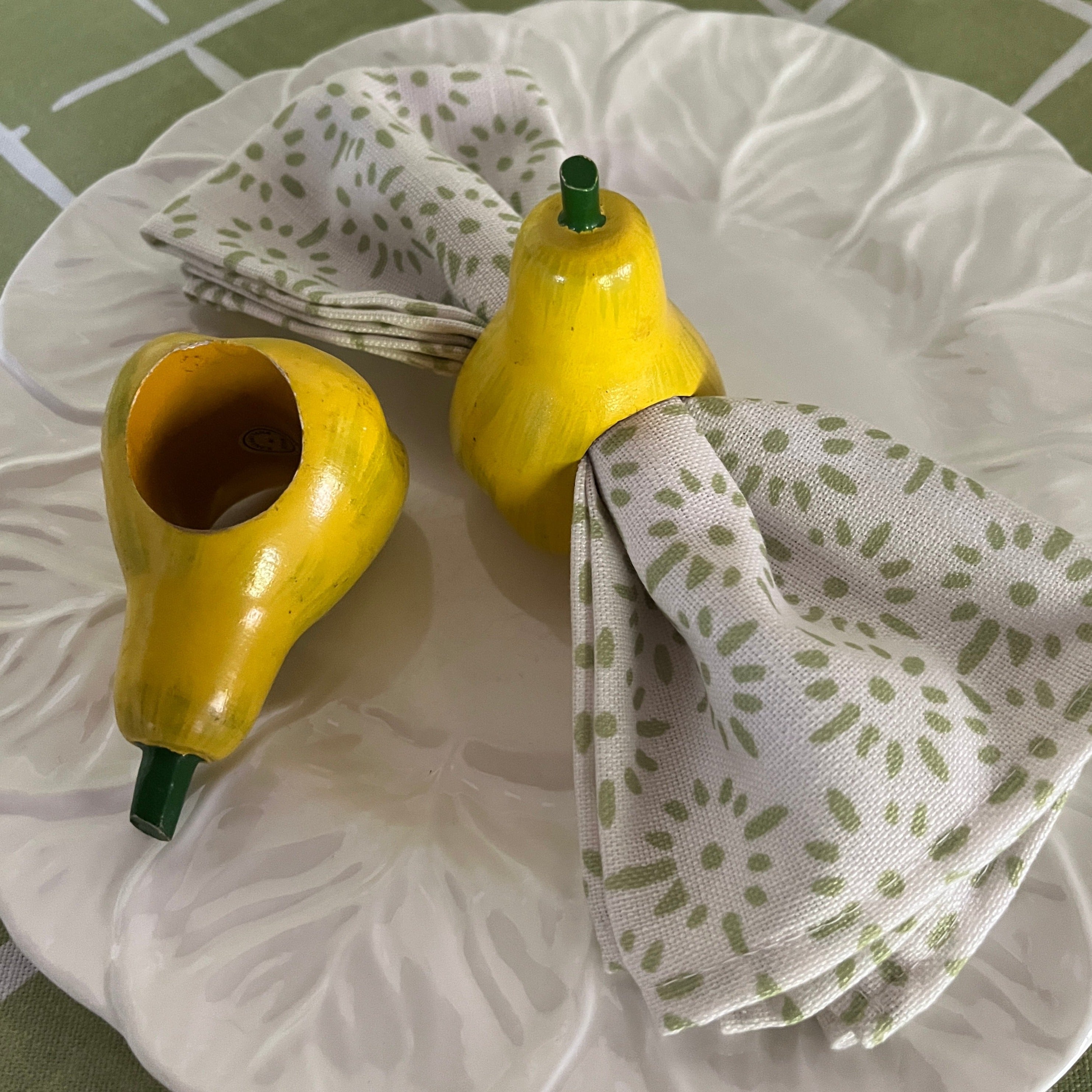 Ceramic pear napkin rings in yellow with green stem, styled with patterned cloth napkins