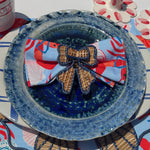 a ceramic blue plate with a bow napkin rin and a lobster napkin on top. 