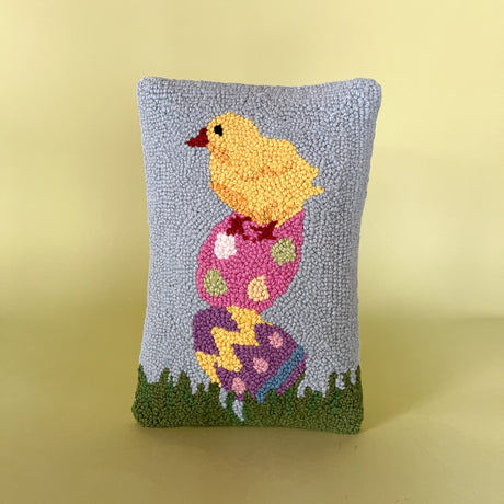 A purple easter pillow with two easter eggs with a yellow chick on top