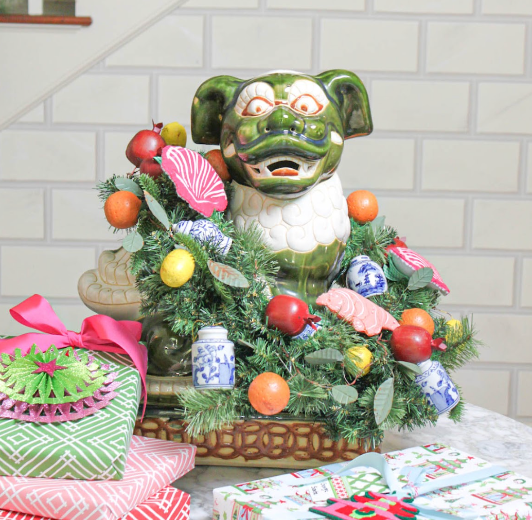 Decorative green foo dog with a chinoiserie Christmas wreath and ornaments on a table.