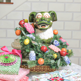 Decorative green foo dog with a chinoiserie Christmas wreath and ornaments on a table.
