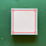 square notepad with pink decorative borders, displayed on a green background