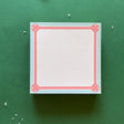 square notepad with pink decorative borders, displayed on a green background