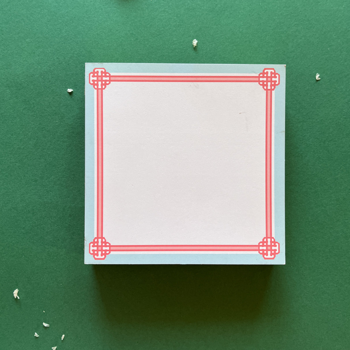 square notepad with pink decorative borders, displayed on a green background