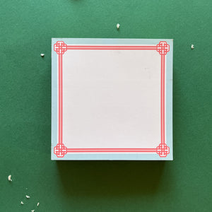 square notepad with pink decorative borders, displayed on a green background