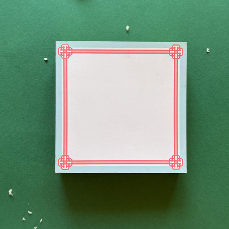 square notepad with pink decorative borders, displayed on a green background