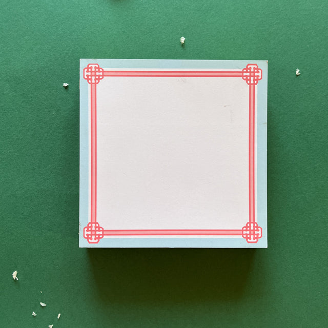 square notepad with pink decorative borders, displayed on a green background