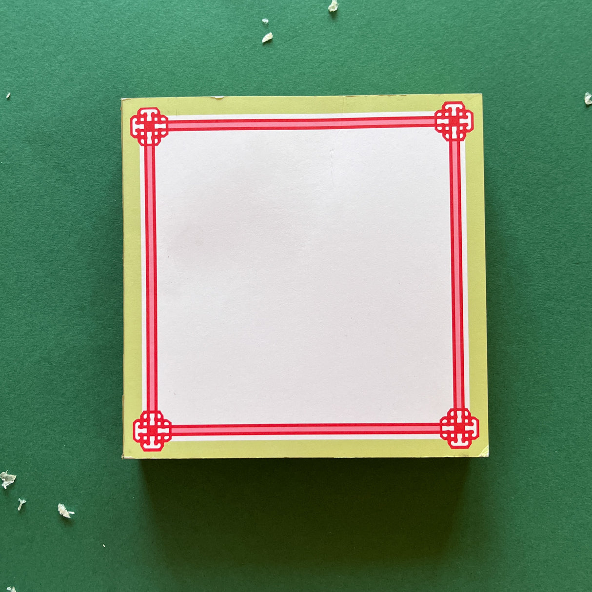 square notepad with red decorative borders, displayed on a green background
