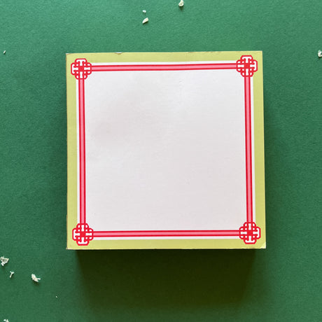 square notepad with red decorative borders, displayed on a green background