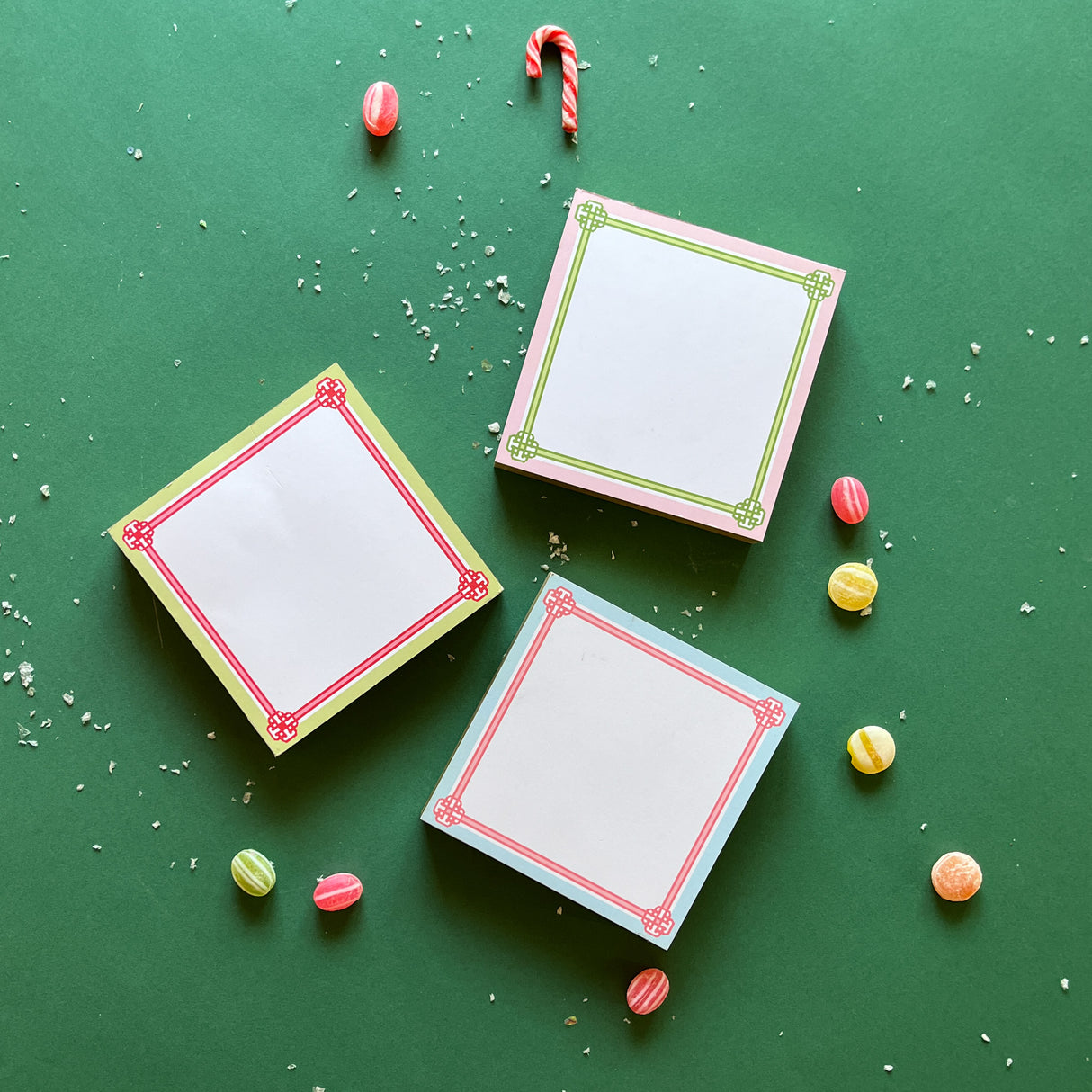 Colorful square notepads with decorative borders, displayed on a green background surrounded by candy canes and decorative balls.