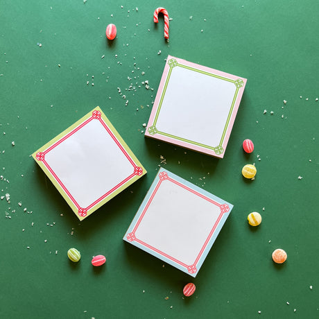 Colorful square notepads with decorative borders, displayed on a green background surrounded by candy canes and decorative balls.