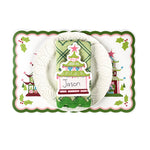 Holiday table setting featuring a Christmas pagoda decorative placemat, white ruffled plate, green patterned napkin, and pagoda-shaped paper place card with handwritten name, arranged on a white background.