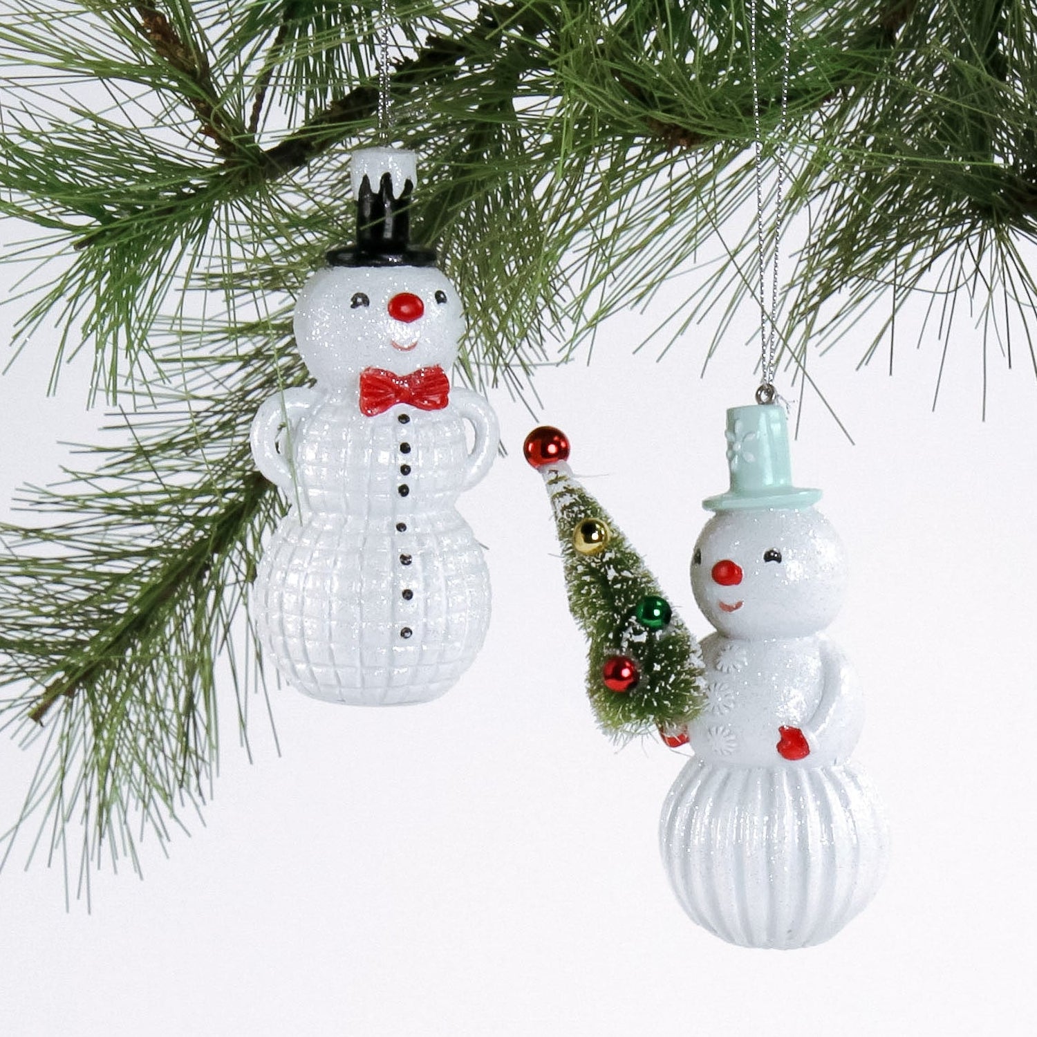 Two snowman ornaments hanging on a Christmas tree branch.