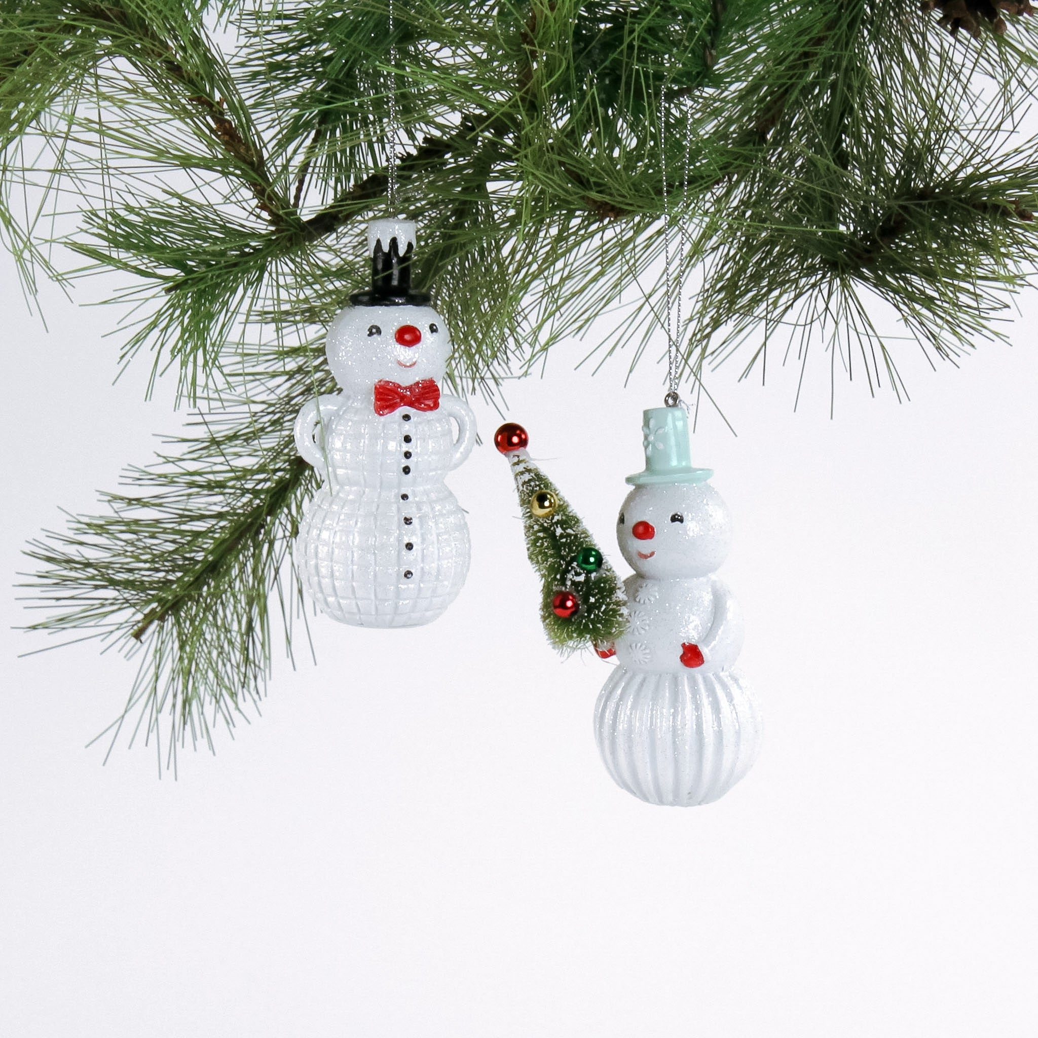 Two snowman ornaments hanging on a Christmas tree branch.