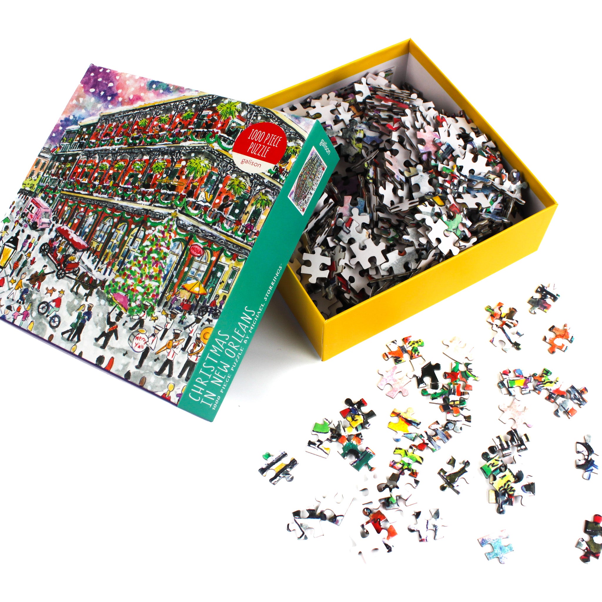 Christmas in New Orleans 1000-piece puzzle by Michael Storrings shown with the box open and colorful jigsaw pieces scattered on a white surface.