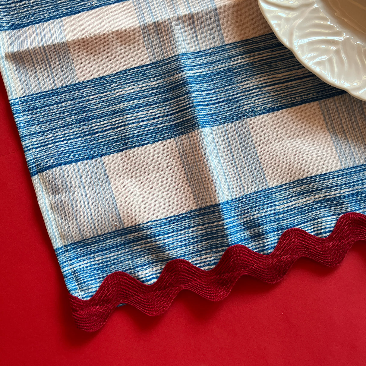 Close-up view of Gin Lane cloth napkin in Swedish Blue with red ric rac trim on red background