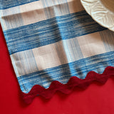 Close-up view of Gin Lane cloth napkin in Swedish Blue with red ric rac trim on red background