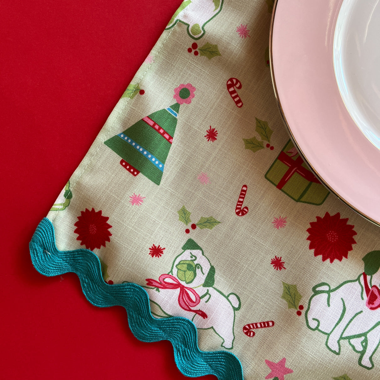 Close-up view of Pug Perfection Christmas cloth dinner napkin and ric rac trim with a pink china plate on top