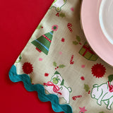 Close-up view of Pug Perfection Christmas cloth dinner napkin and ric rac trim with a pink china plate on top