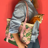 Close-up side view of a model holding the Jungle Road large canvas tote in pink and green with a toy giraffe sticking out of the tote.