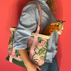 Close-up side view of a model holding the Jungle Road large canvas tote in pink and green with a toy giraffe sticking out of the tote.