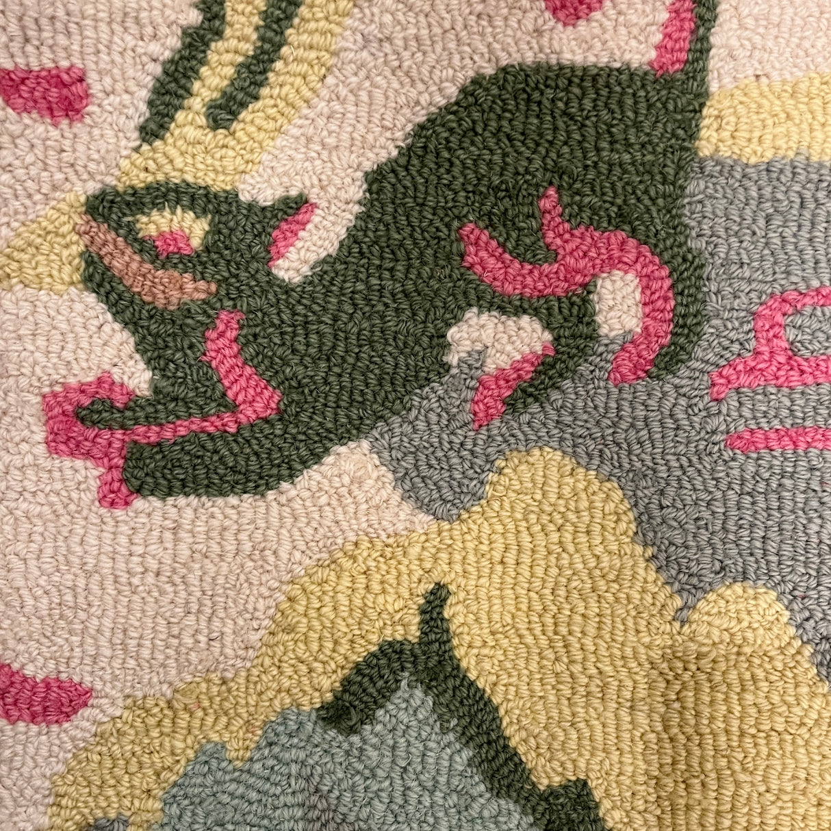 A close up of a pink and green rug focussing on a green animal motif. 