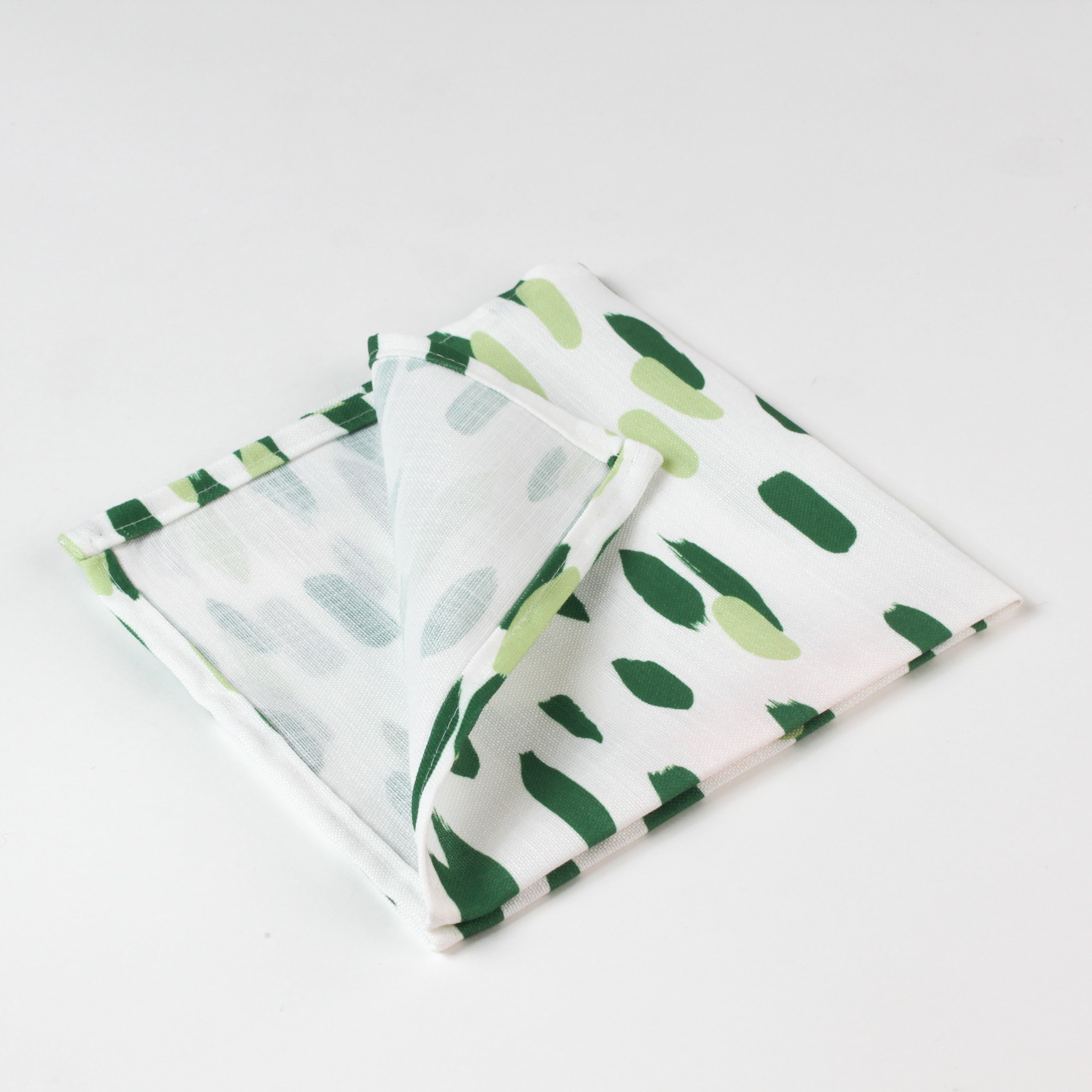 Close-up of folded cloth napkin with a green brushstroke pattern on white fabric.