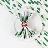 Green brushstroke patterned cloth napkin styled on a white plate with a red floral napkin ring.