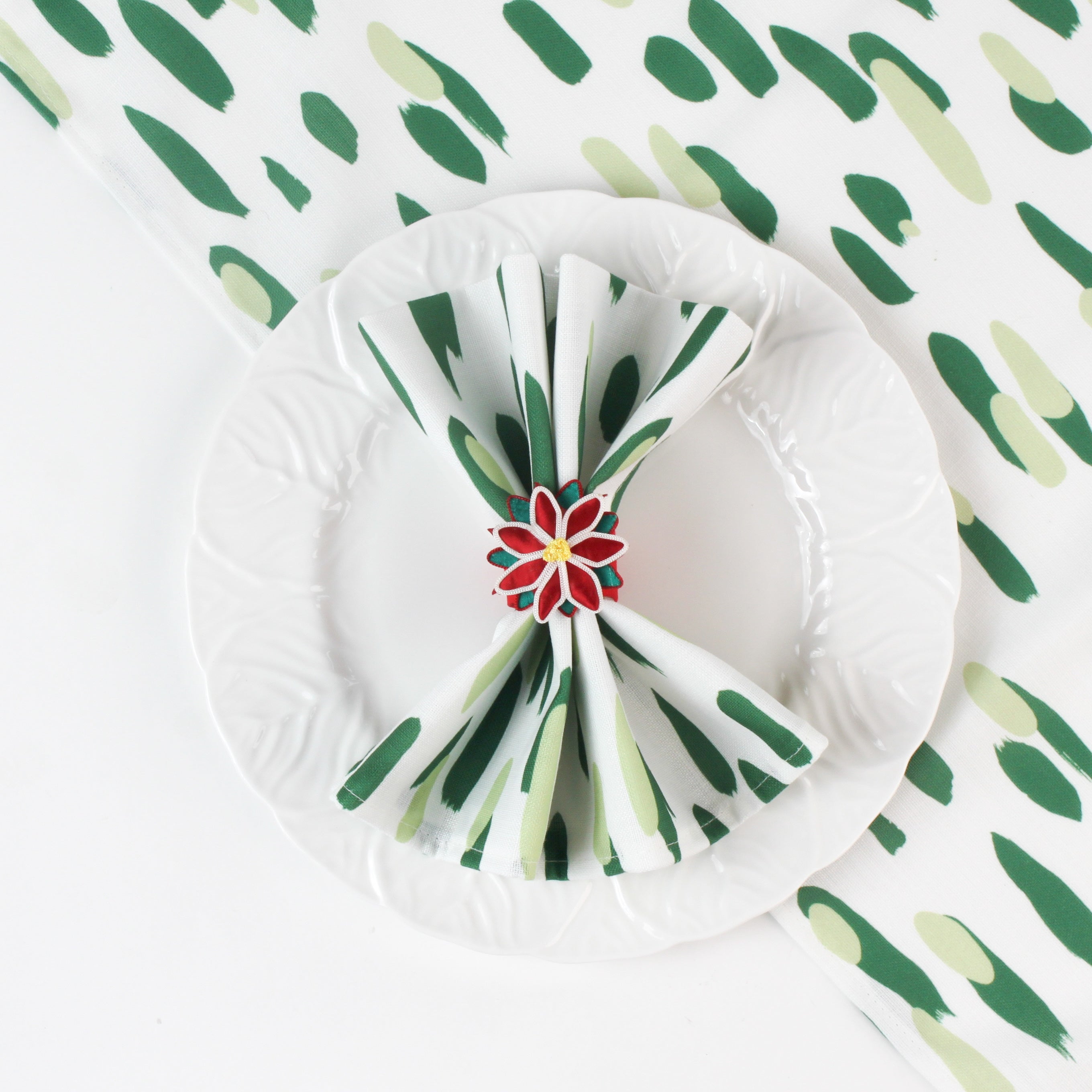 Green brushstroke patterned cloth napkin styled on a white plate with a red floral napkin ring.