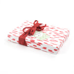 Side view of gift wrapped in red brushstroke wrapping paper with red ribbon and green gift tag.