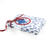 Side view of gift wrapped in blue brushstroke wrapping paper with red ribbon and tags.
