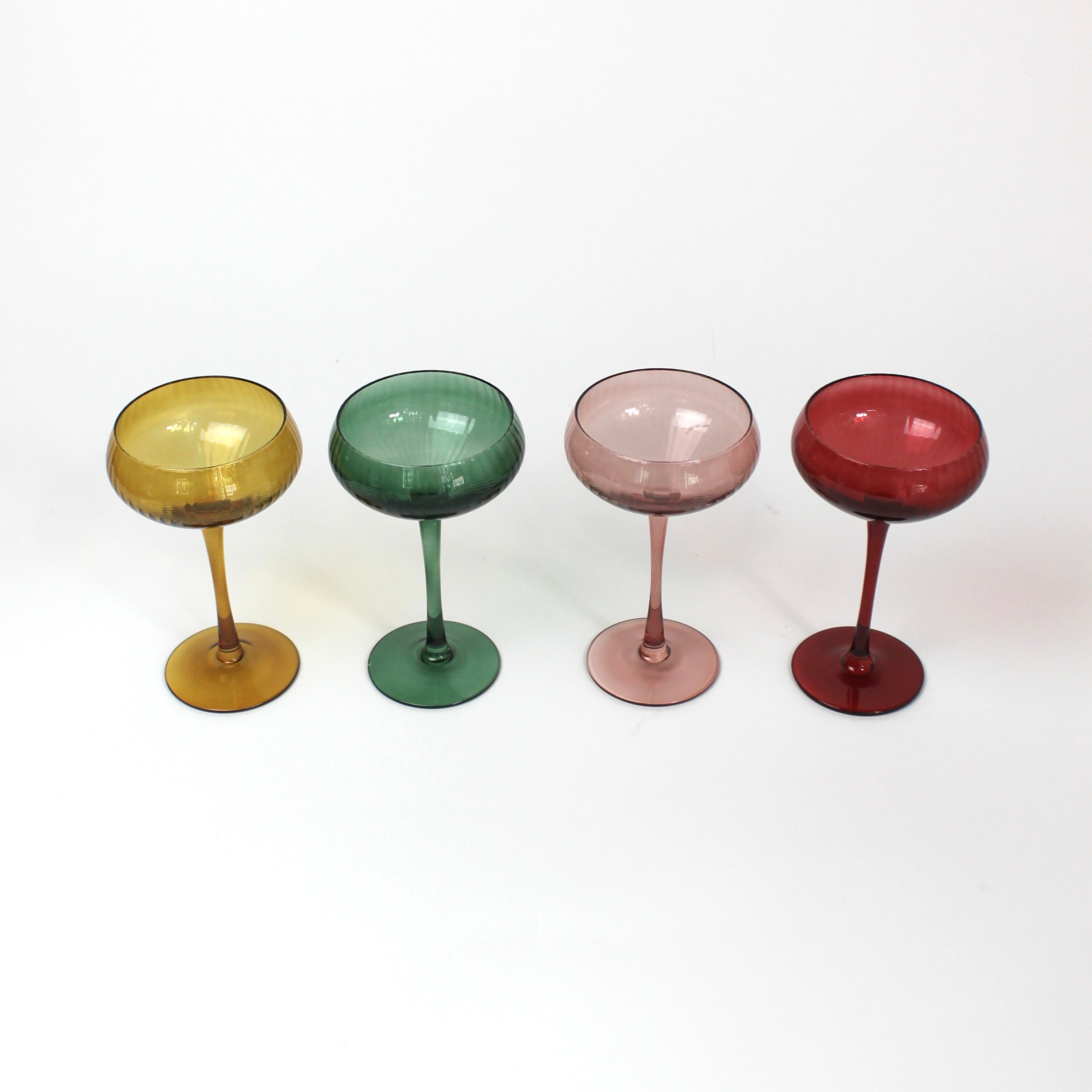 Four colorful cocktail glasses in yellow, green, pink and red on a white background