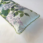 a corner detail of a light blue throw pillow made from hydrangea print fabric and green cord piping.