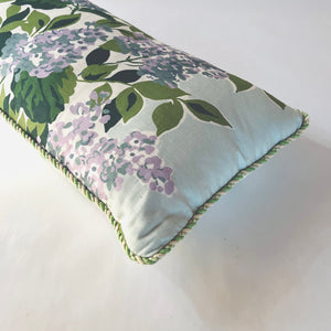 a corner detail of a light blue throw pillow made from hydrangea print fabric and green cord piping. 