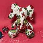 White stuffed elephant toy with red and green floral pattern and green bow in a red ackground.