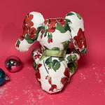 White stuffed elephant toy with red and green floral pattern and green bow back in a red background.